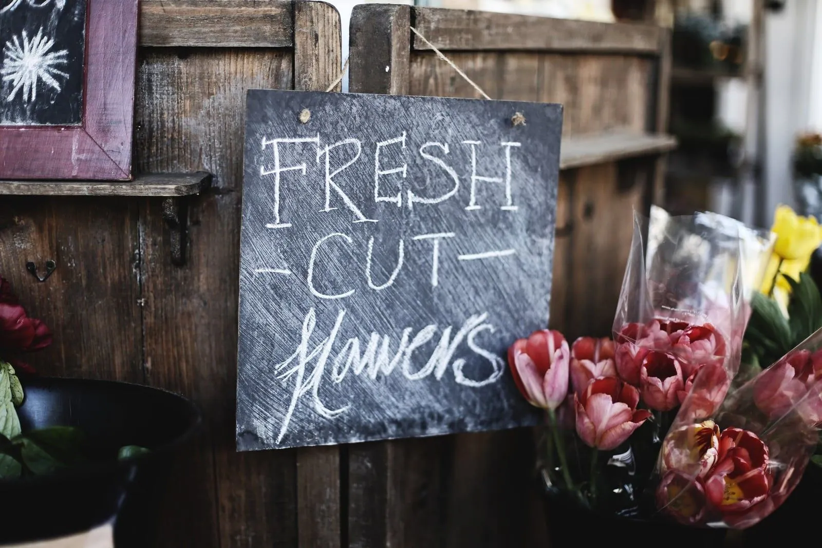 Ardoise « Fresh Cut Flowers » accrochée à un établi en bois, entourée de tulipes fraîchement coupées